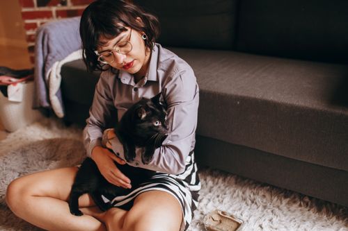 Free Woman holding a black cat while sitting on a cozy rug indoors. Stock Photo