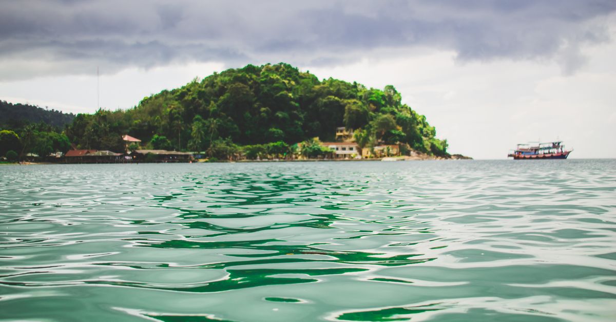 Scenic view of a lush island surrounded by green waters and a distant boat in Thailand.