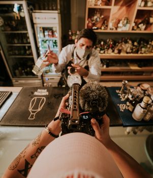 A bartender mixes a cocktail while being filmed in a cozy bar setting, capturing the scene from above.