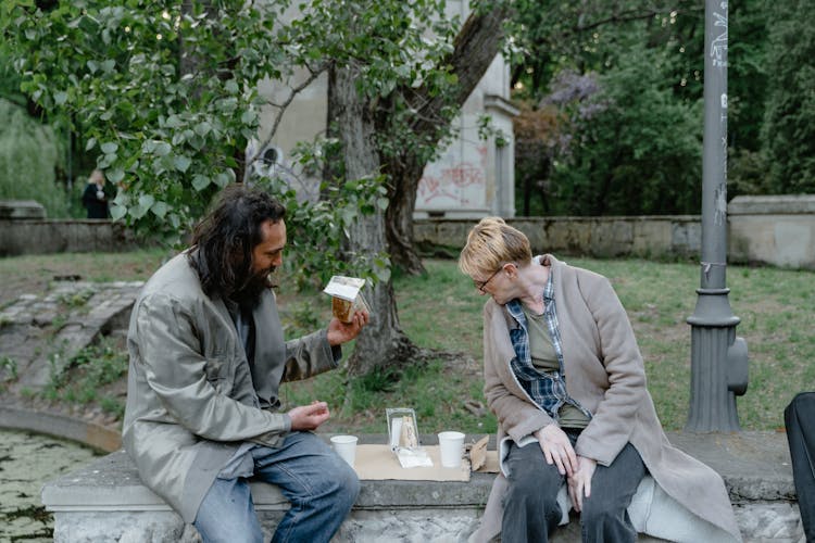 Two Homeless People Eating On Sandwiches