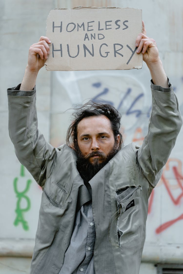 Man In Gray Jacket Holding A Brown Cardboard Poster