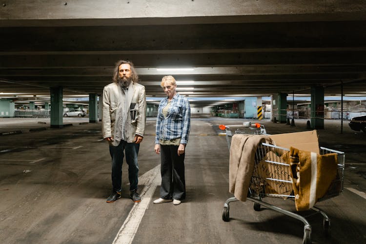 A Homeless Man And Woman At A Parking Lot 