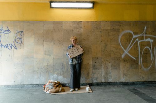 Free A senior woman stands with a 'HELP' sign in an urban area, symbolizing poverty and homelessness. Stock Photo
