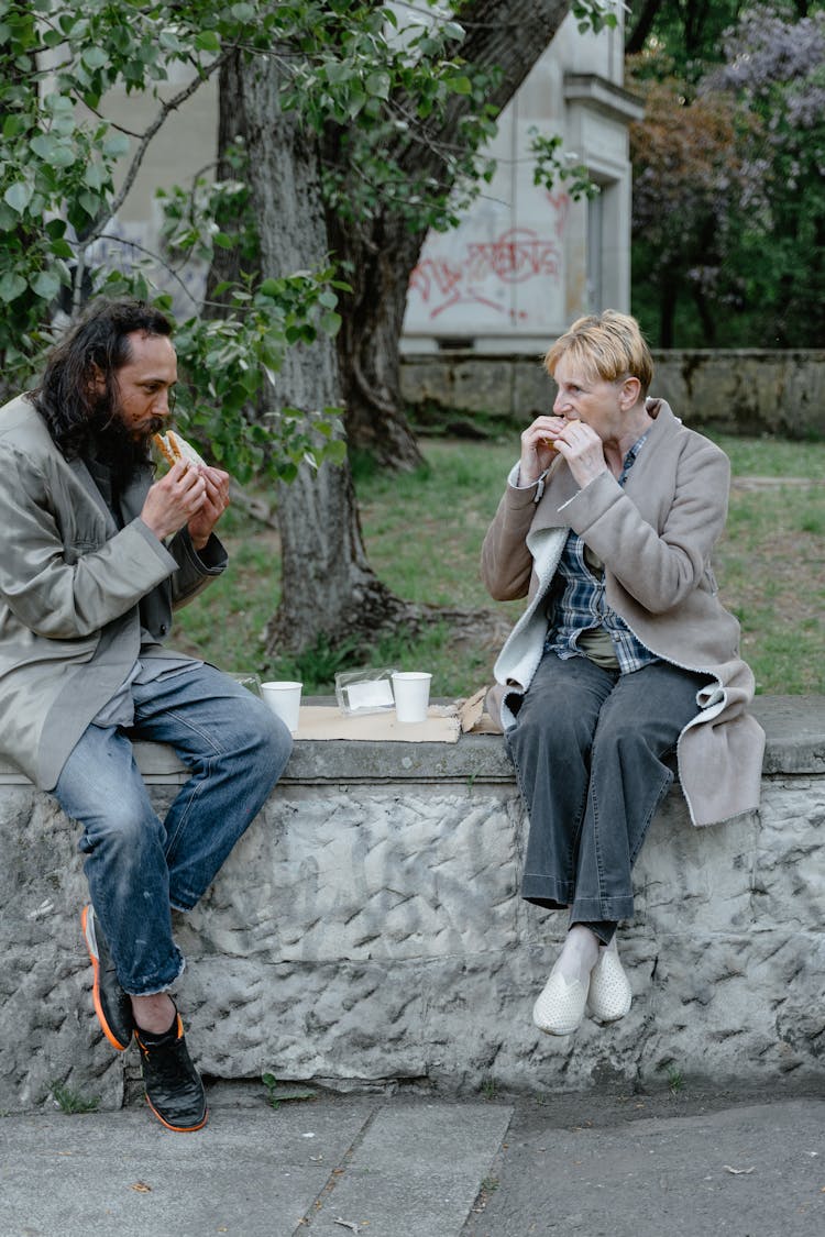 Two Homeless People Eating Sandwich Together