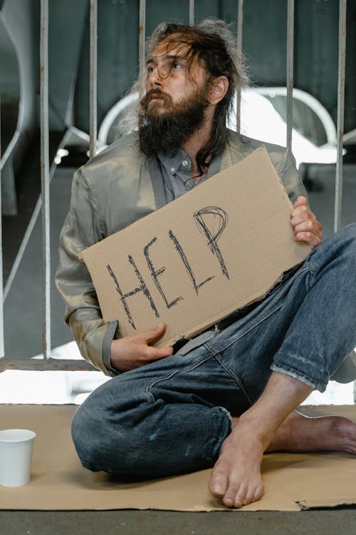 Free A Male Beggar Sitting on a Ground while Holding a Help Banner Stock Photo