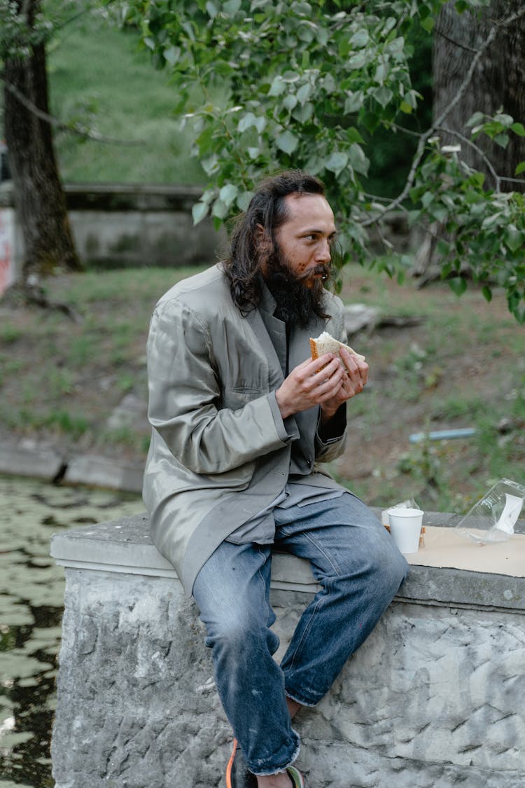 A Man In Gray Jacket Eating A Sandwich
