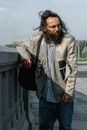 Man in White Jacket and Blue Denim Jeans Standing Near Gray Wooden Fence