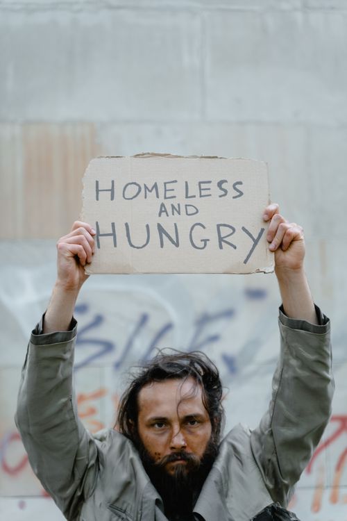 Free A bearded homeless man holds a sign reading 'Homeless and Hungry' against a graffiti wall. Stock Photo