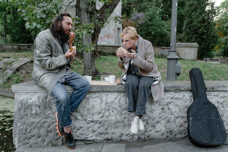 Elderly People Sitting On Concrete Bench While Eating Together