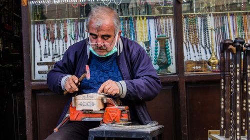 Free A senior artisan skillfully crafting handmade jewelry at an outdoor market stall. Stock Photo