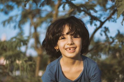 Free Joyful child smiling brightly in a sunny outdoor setting, surrounded by nature. Stock Photo