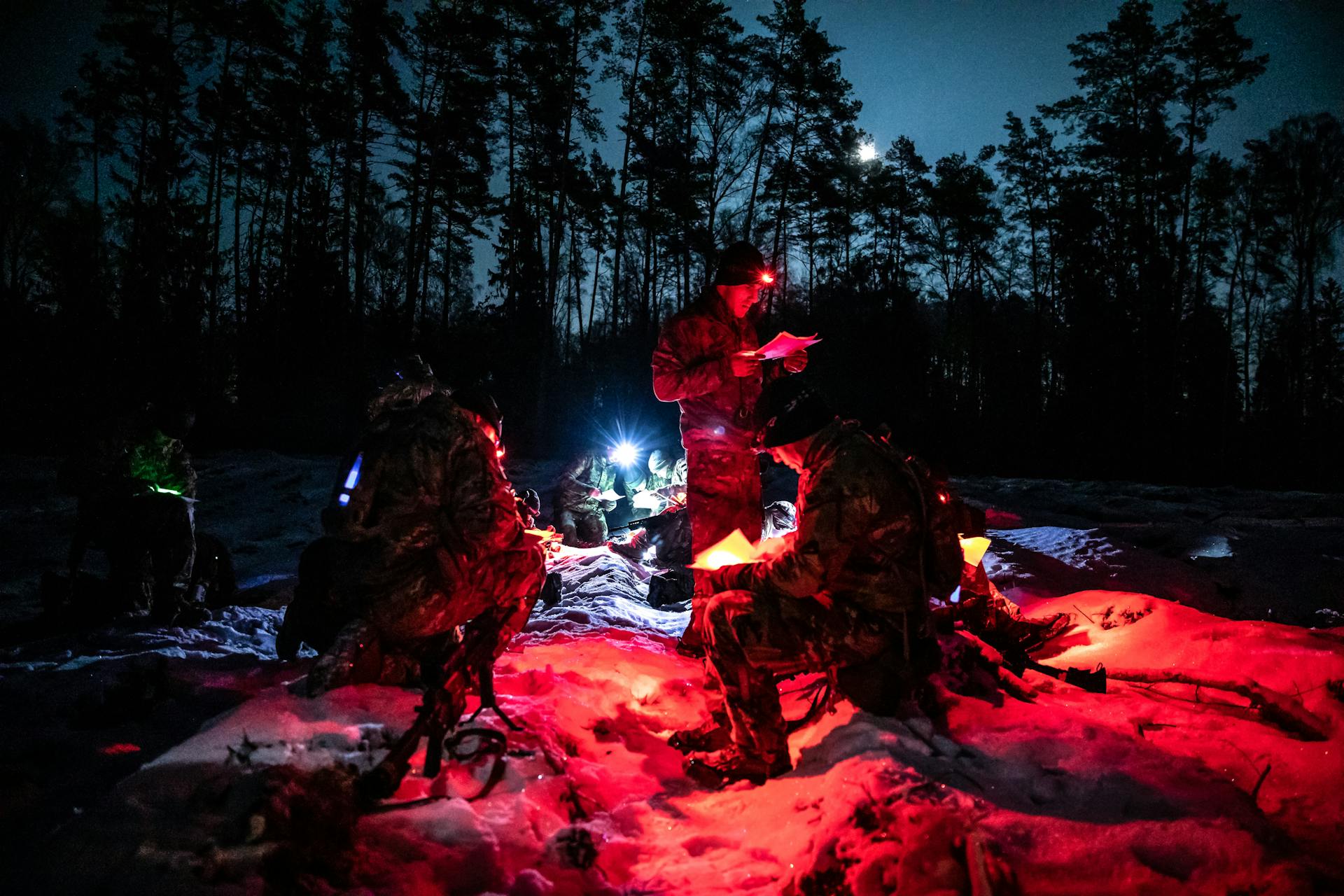 Soldiers engage in night training, reading maps by red light in snowy Polish forest.