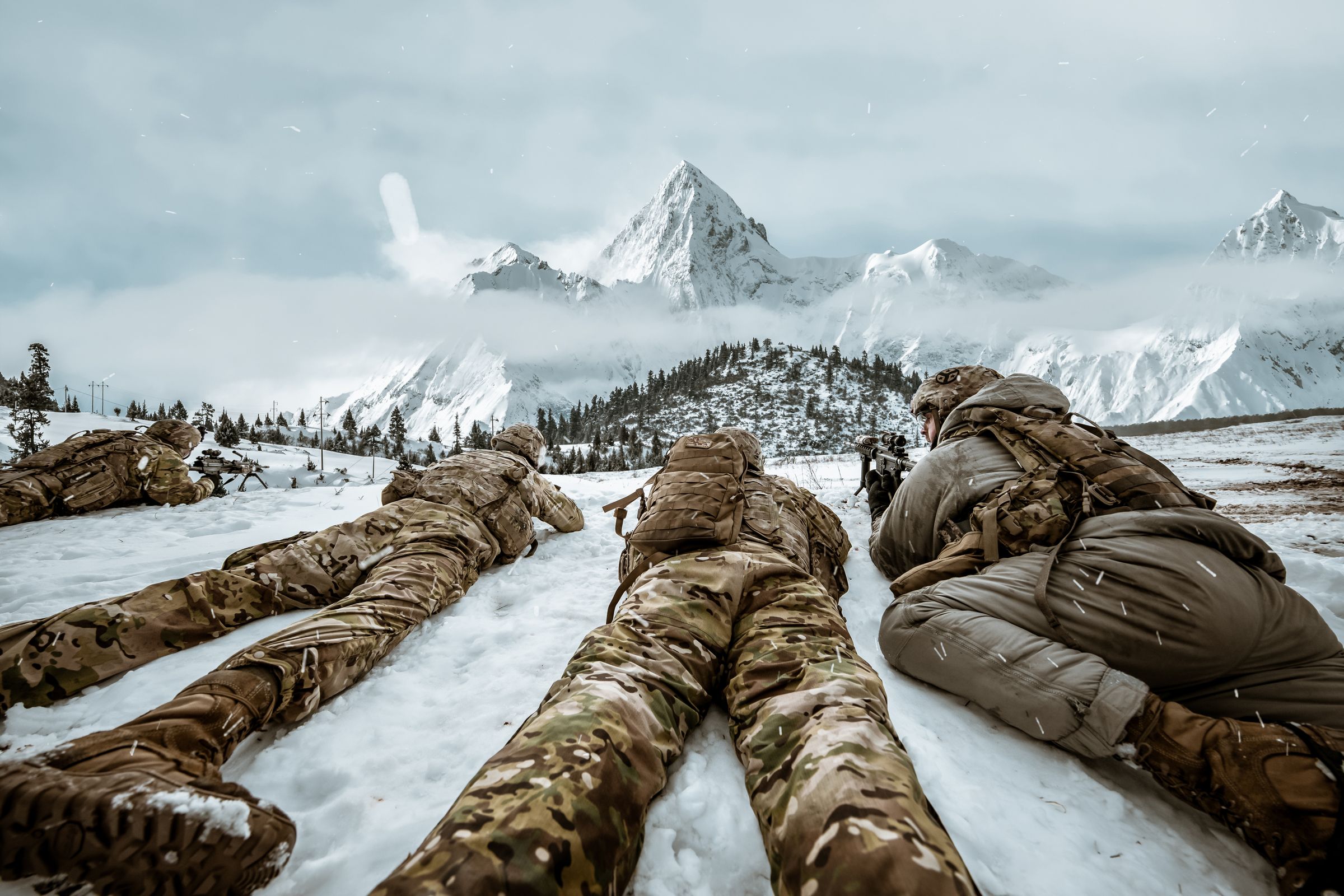 Tactical team in overwatch on a snow ridge below arctic peaks