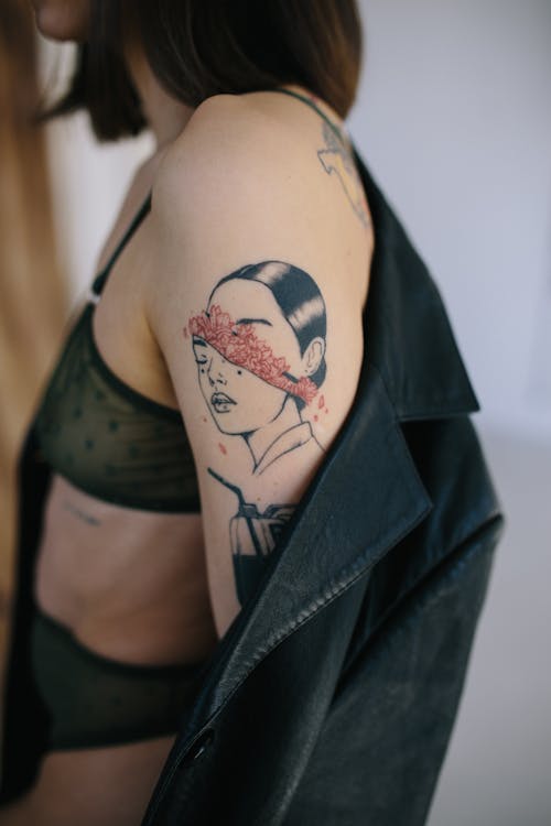 Crop tattooed woman putting on gray coat