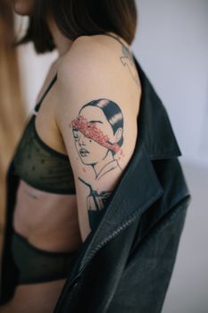 Side view of crop anonymous female with tattoo on arm wearing black underwear and taking on gray woolen coat