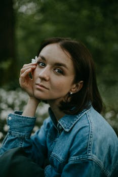 Portrait of a woman with short hair and flower in denim jacket in nature, exuding a moody vibe.