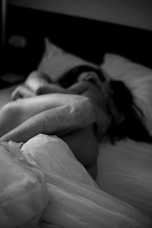 Black and white of unrecognizable naked embracing couple lying on soft blanket in bed