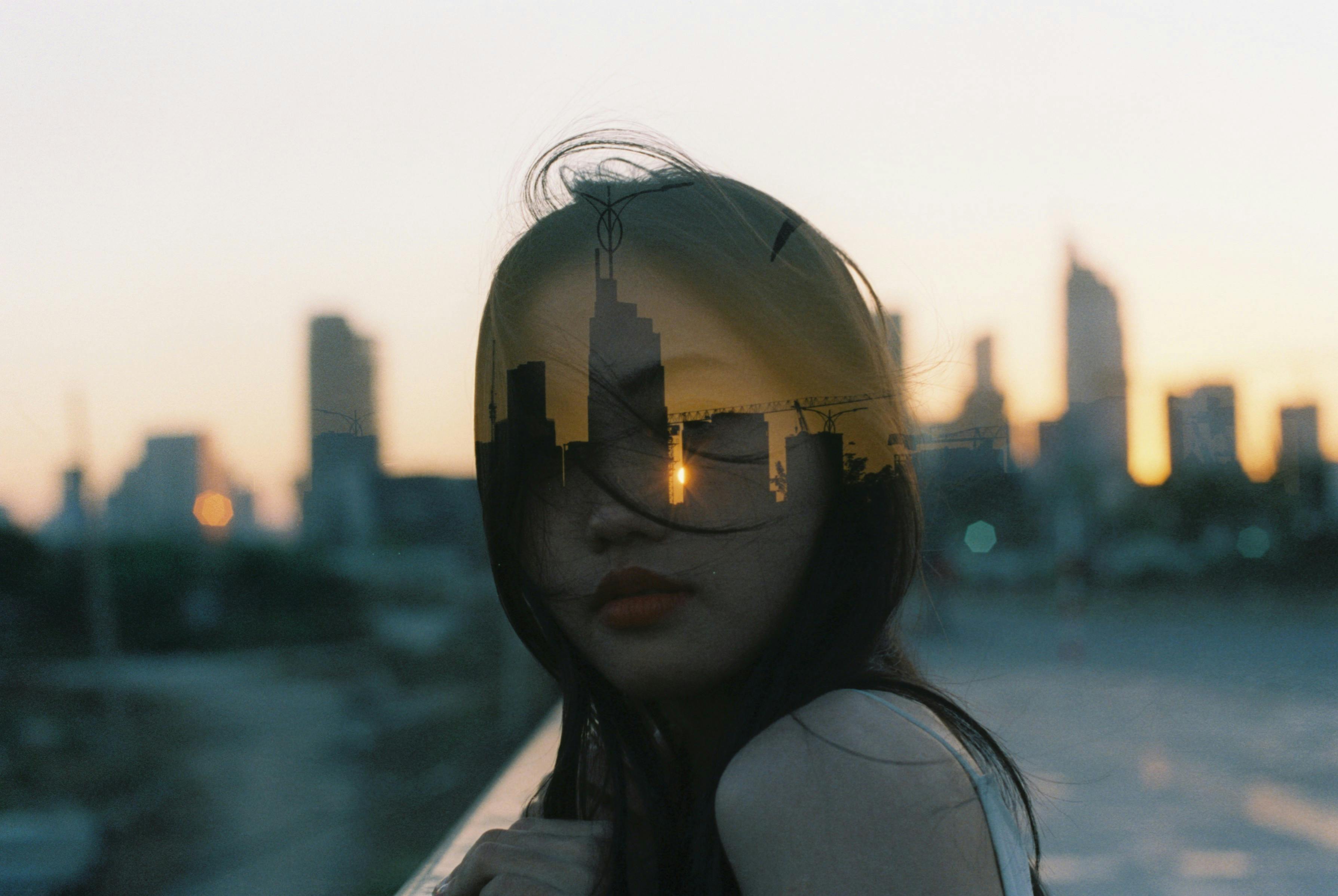 Artistic double exposure of a young woman and city skyline at dusk in Vietnam.