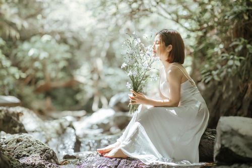 Free A woman in a white dress serenely holding a bouquet, surrounded by lush forest greenery. Stock Photo