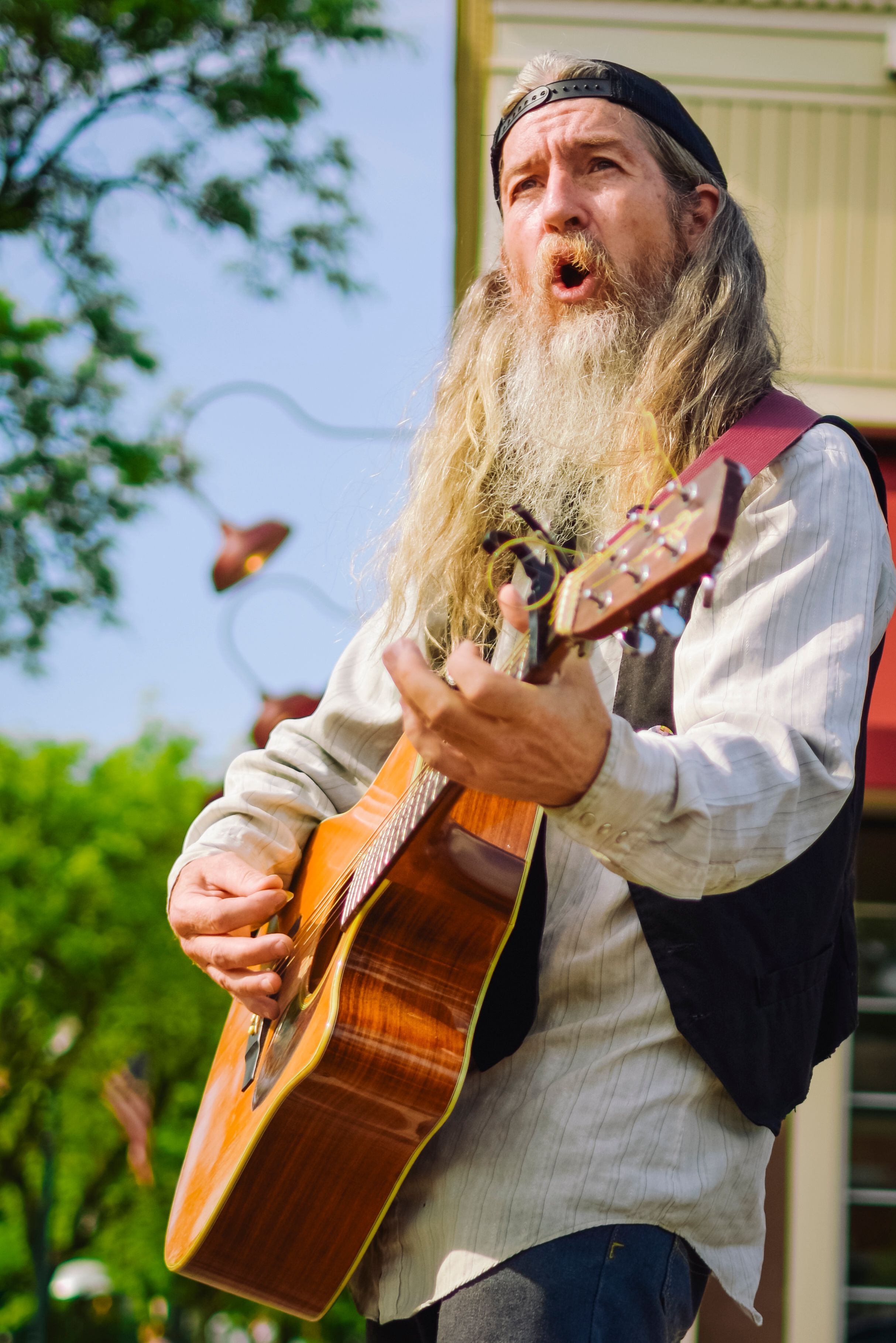 Elderly bearded musician passionately plays acoustic guitar outdoors in a park.