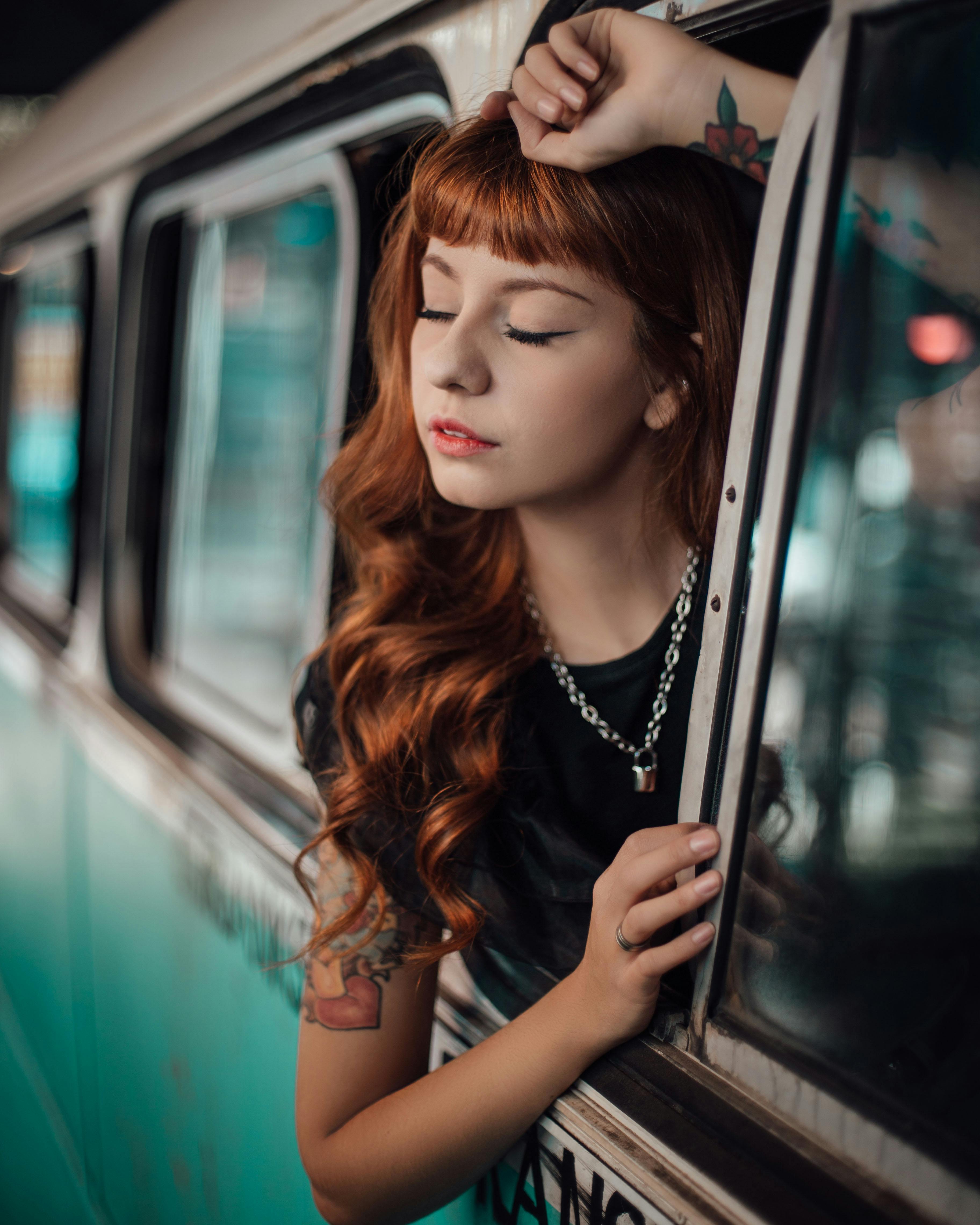 A young woman with curly hair and tattoos poses thoughtfully in a vintage vehicle, creating a nostalgic feel.