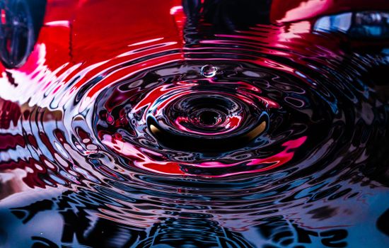 Close-up of a droplet creating vibrant ripples with colorful reflections.