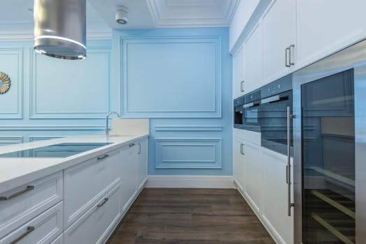 Sleek modern kitchen featuring white cabinetry, blue accent wall, and stainless appliances.