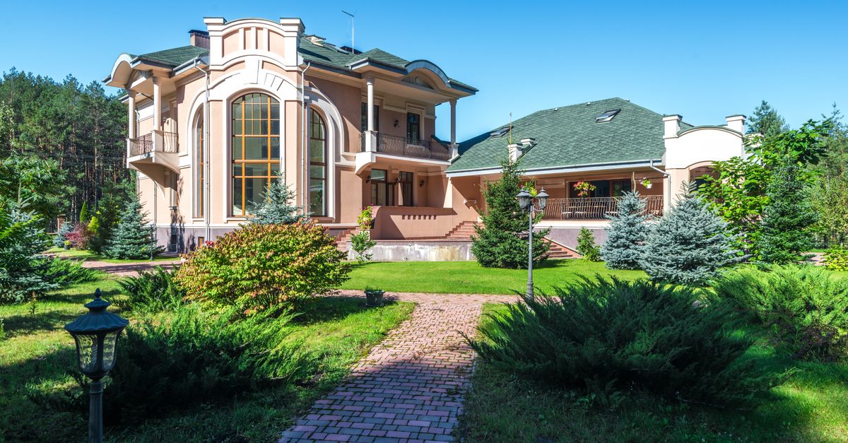 Beautiful mansion in sunny weather, surrounded by lush greenery and a clear blue sky.