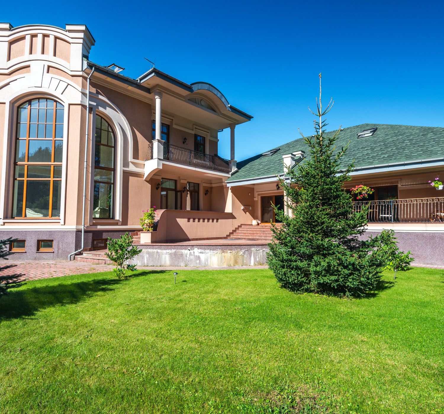 Modern luxury villa with large windows, surrounded by lush green lawn and trees.