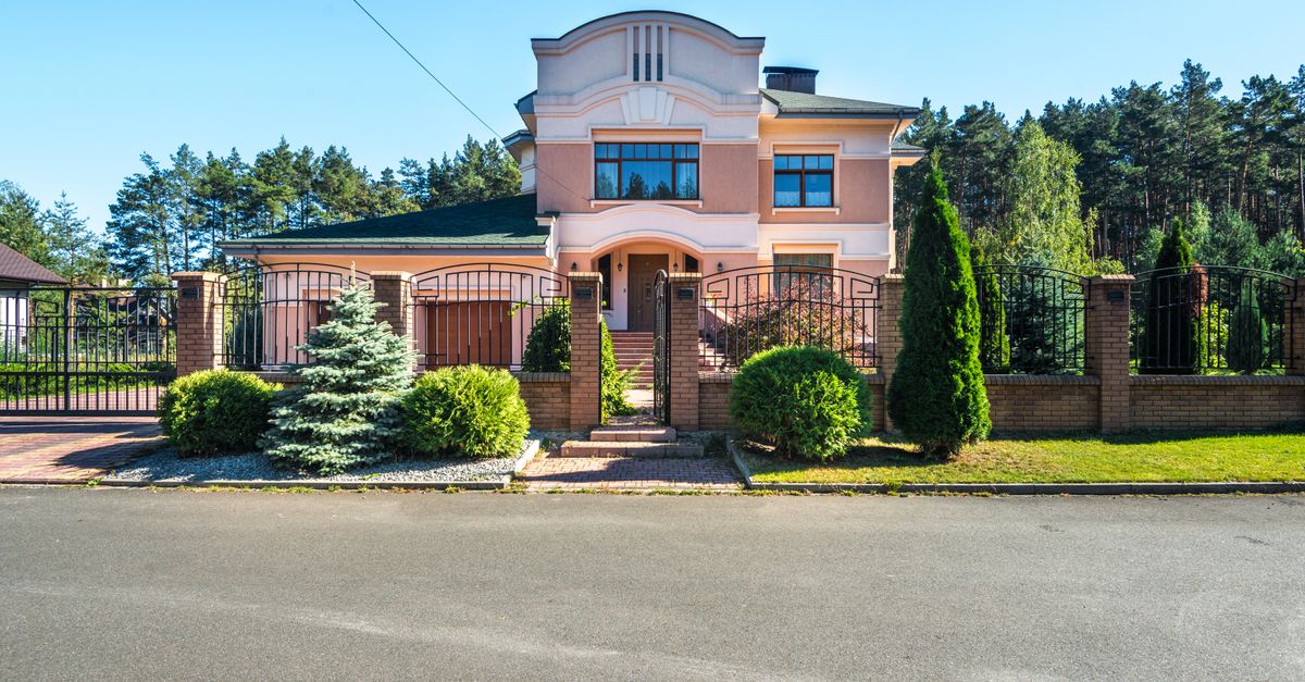 Beautiful luxury suburban house with landscaped garden and gated entrance on a sunny day.