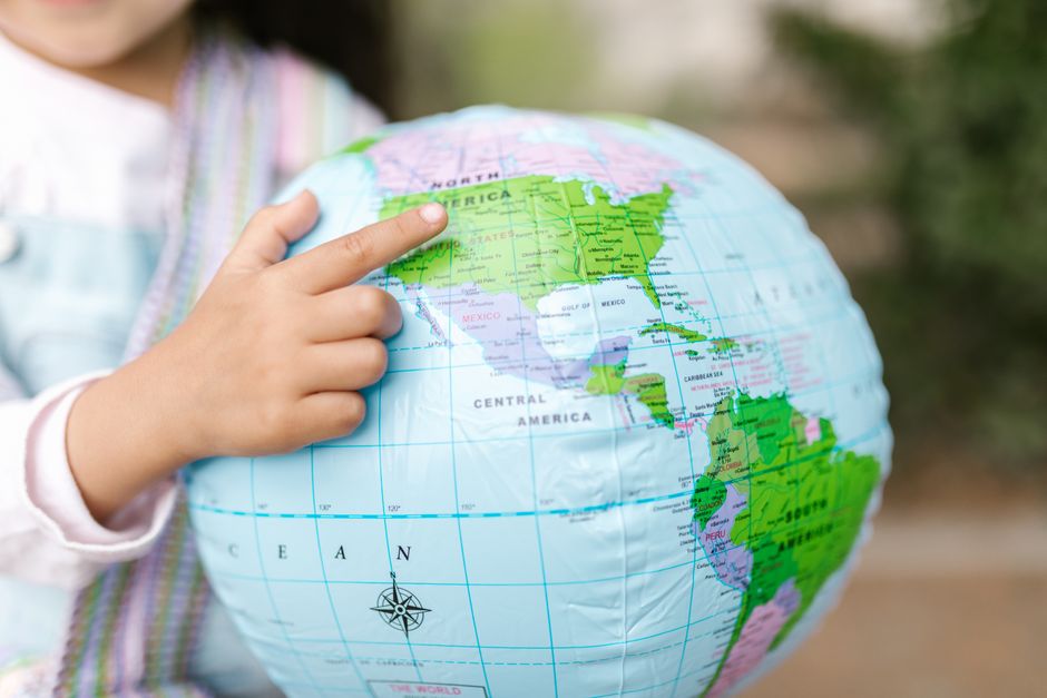 A young child points to North America on a colorful inflatable globe, highlighting exploration and education.