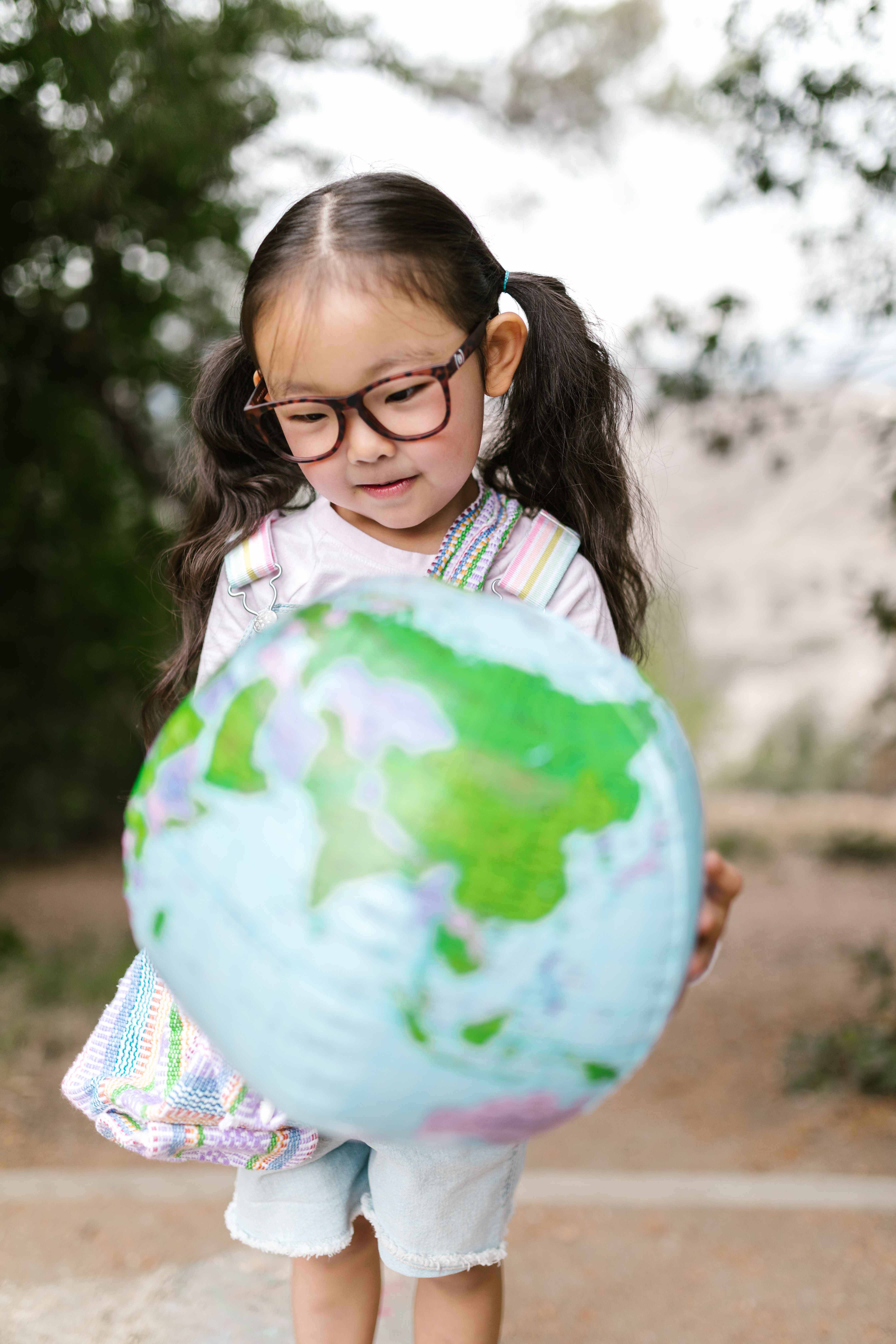 A young girl explores the world with a globe in a natural outdoor environment.