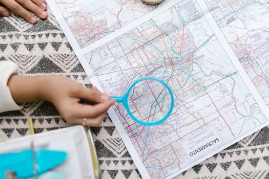 A top view of a hand holding a magnifying glass over a map, emphasizing exploration.