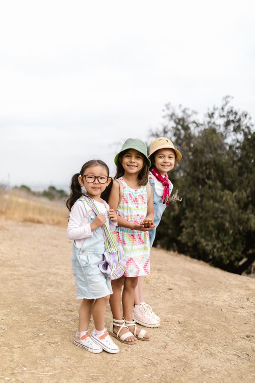 Free Three smiling children enjoying a spring day outside with a cloudy sky. Stock Photo