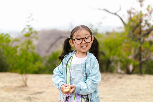 Free A cheerful young girl wearing glasses smiles while holding a toy outdoors. Stock Photo