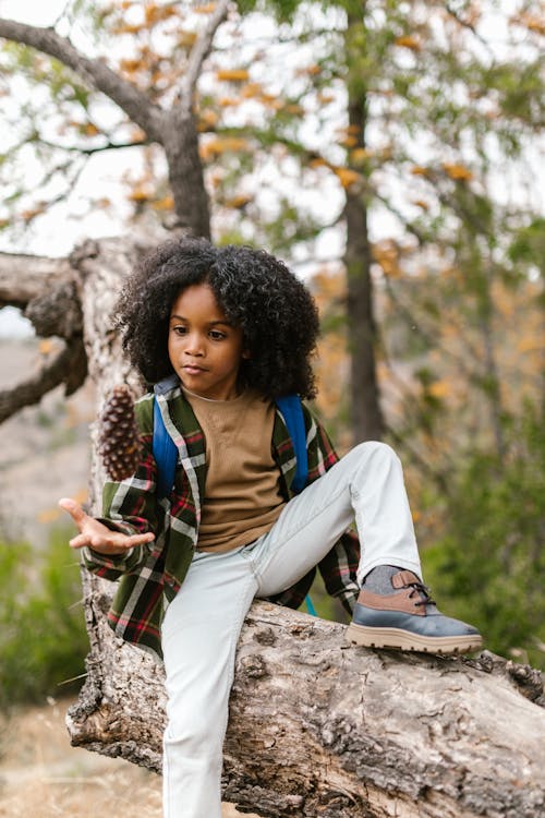 A Boy Sitting on a Tree Trunk while Looking at the Toy in the Air