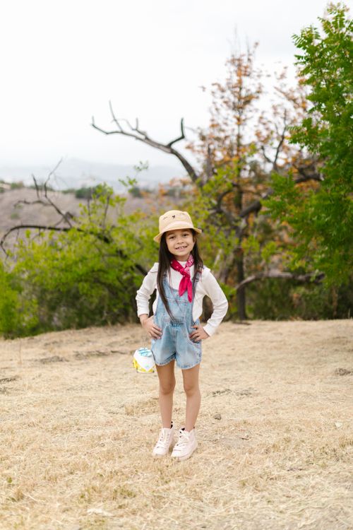 Free Smiling girl in overalls and bucket hat enjoying outdoor exploration. Stock Photo