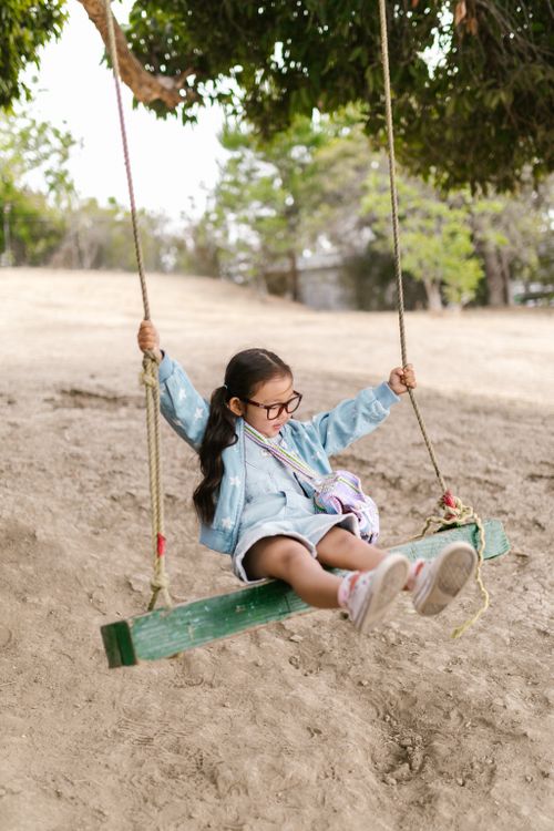 Free A young girl in a blue jacket swings joyfully in a sunny park, capturing the essence of childhood play. Stock Photo