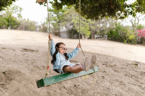 Free Young girl enjoying a playful moment on a swing in a natural setting, expressing joy and freedom. Stock Photo
