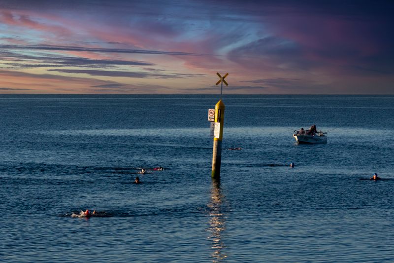 Peaceful scene of swimmers and a boat at sunset on Williamstown Beach, Australia.