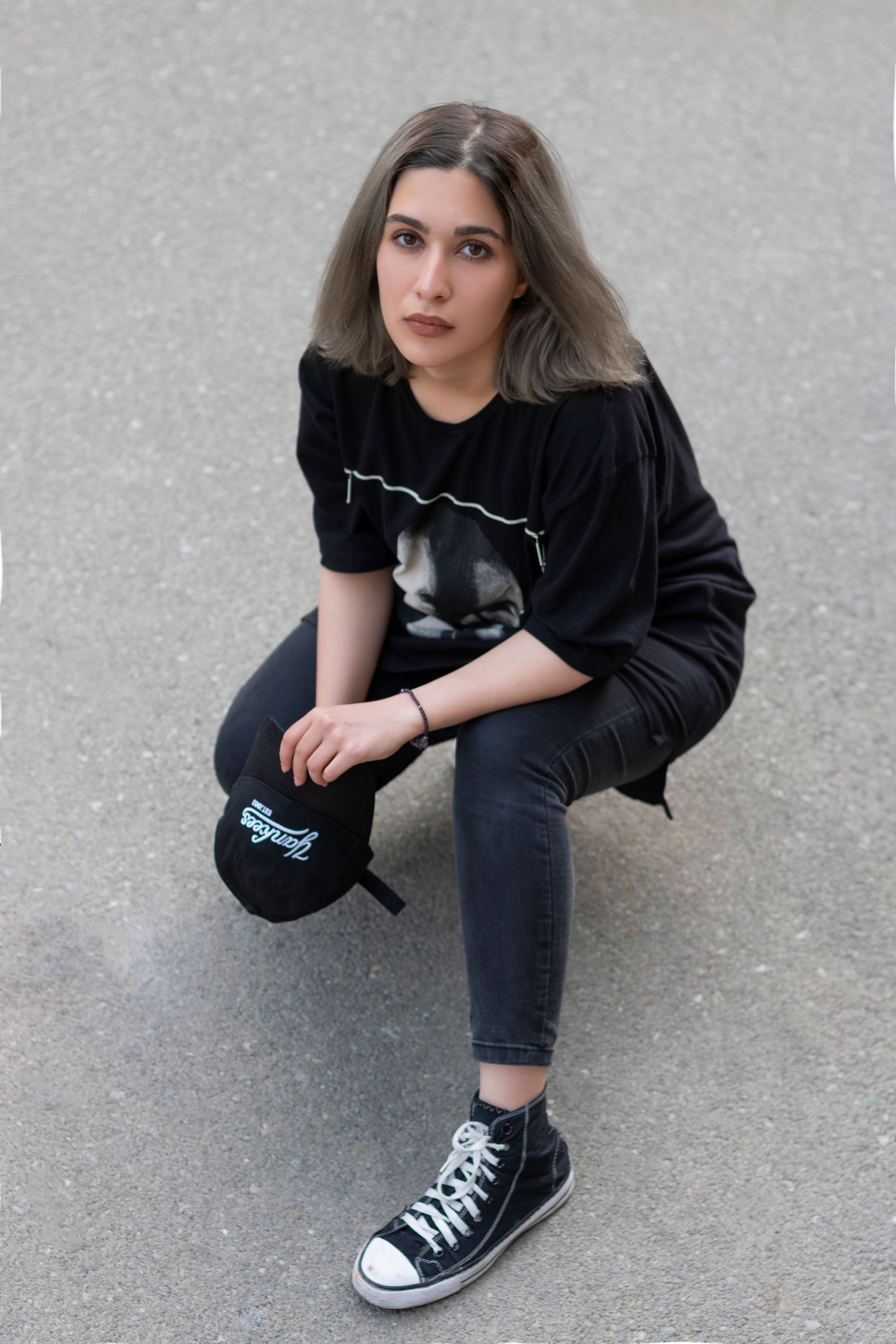 Portrait of a stylish young woman in black streetwear crouching on a urban sidewalk.