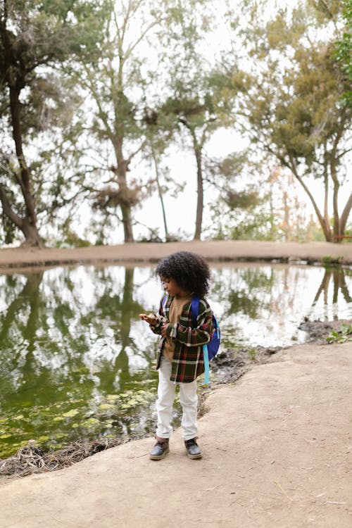 A Little Boy in Plaid Long Sleeves Standing Near a Lake