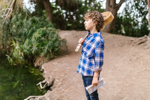 Free A boy with curly hair wearing plaid holding a ukulele outdoors by a stream. Stock Photo
