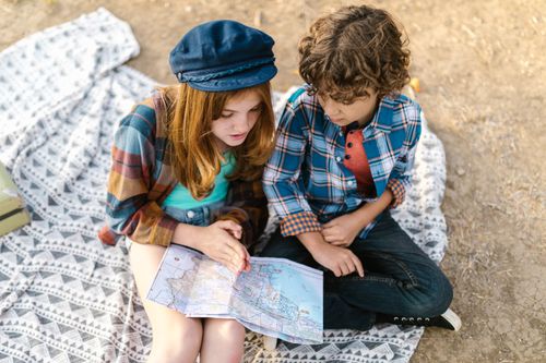 Free Two children exploring a map while sitting on a picnic blanket outdoors, capturing the essence of adventure and learning. Stock Photo