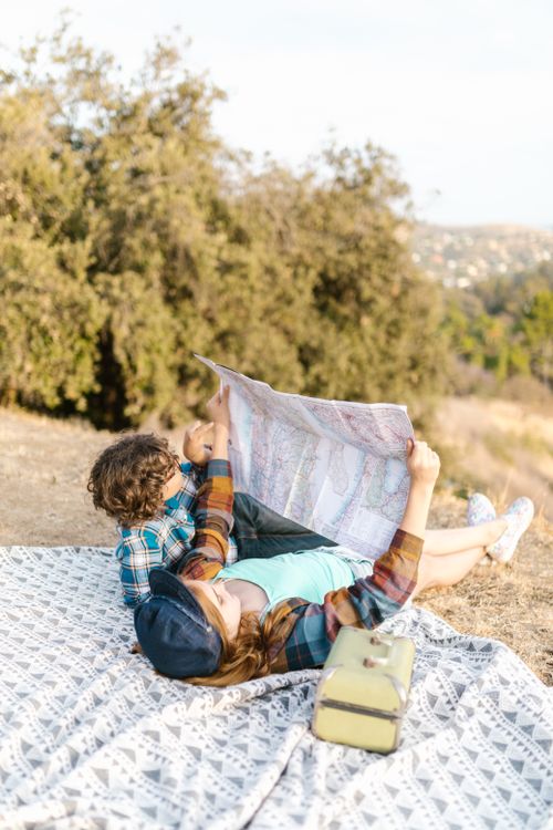 Free Two teenagers lying on a picnic blanket outdoors, exploring a map for travel planning. Stock Photo