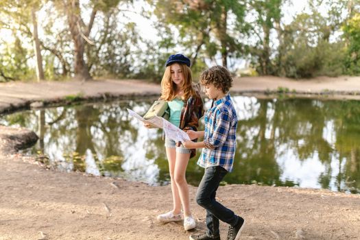 Two children exploring a scenic lake path with a map under the bright daylight.
