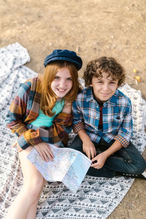 Free Two children in plaid shirts enjoying a picnic outdoors, looking at a map and smiling. Stock Photo