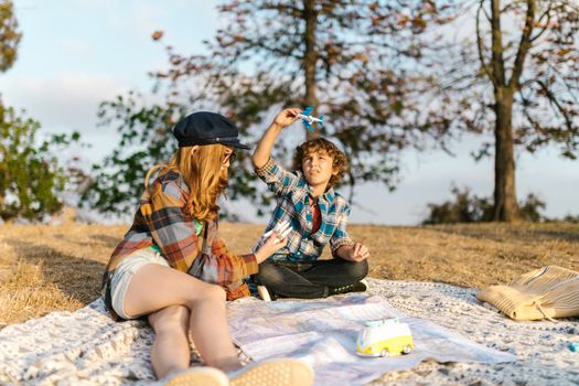 Two children playing with toys on a picnic blanket outdoors during a sunny day.