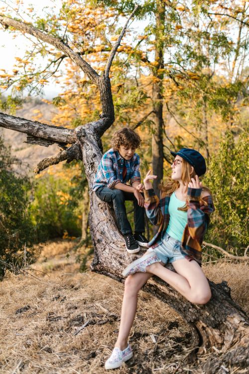 Free Two kids in casual outfits playing on a tree branch in a vibrant autumn forest setting. Stock Photo