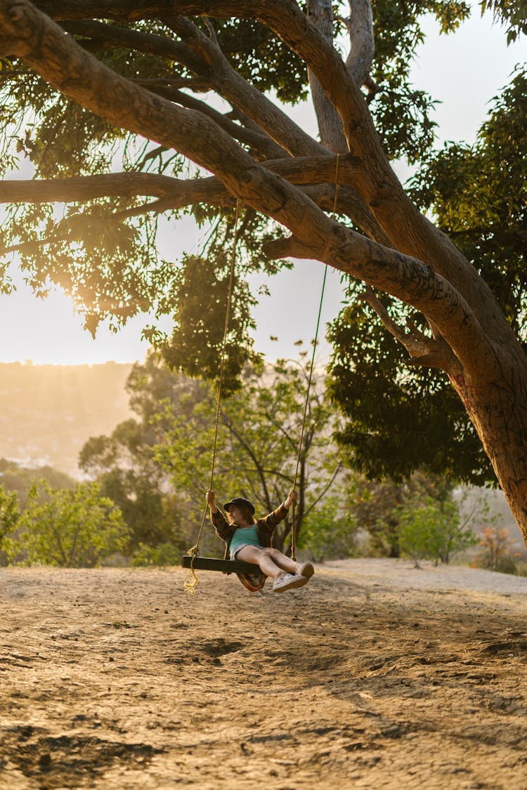 A Girl Riding A Swing Under A Tree